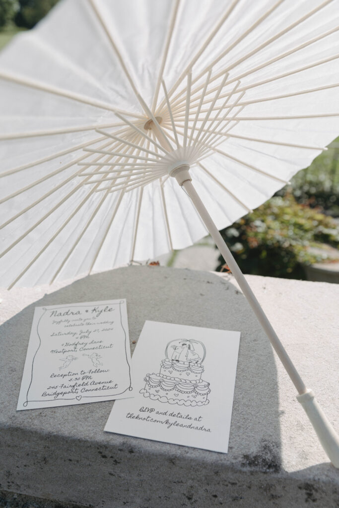 Documentary and editorial wedding photography from garden summer outdoor wedding at Eolia Mansion in Connecticut. Photos taken by Suz Lundeen Photo - destination wedding, family, and maternity photographer based in New England and the Midwest. Photo of hand drawn wedding invites in a wedding flat lay with a parasol.