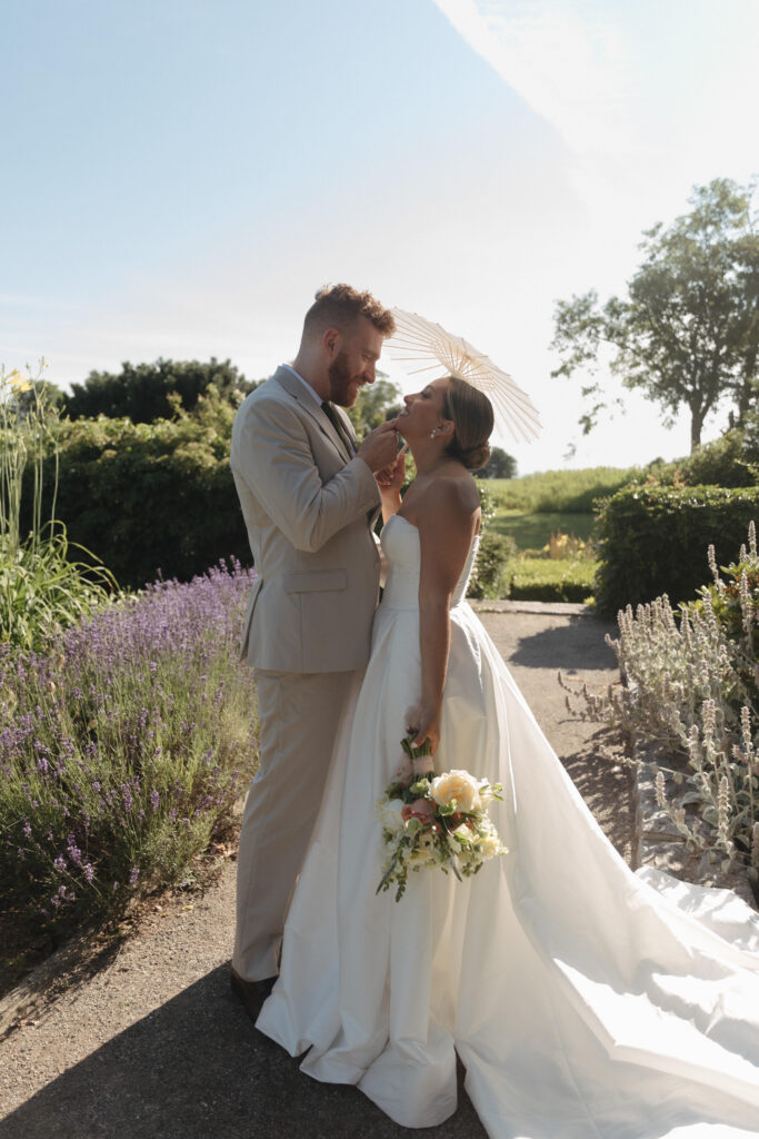 Documentary and editorial wedding photography from garden summer outdoor wedding at Eolia Mansion in Connecticut. Photos taken by Suz Lundeen Photo - destination wedding, family, and maternity photographer based in New England and the Midwest. Photo of bride and groom with parasol at their garden wedding in direct afternoon sunlight.