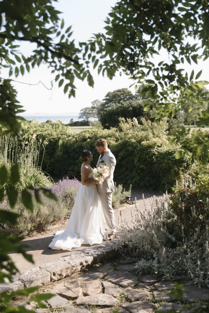 Documentary and editorial wedding photography from garden summer outdoor wedding at Eolia Mansion in Connecticut. Photos taken by Suz Lundeen Photo - destination wedding, family, and maternity photographer based in New England and the Midwest. Photo of bride and groom embracing in the wild whimsy garden at Eolia.