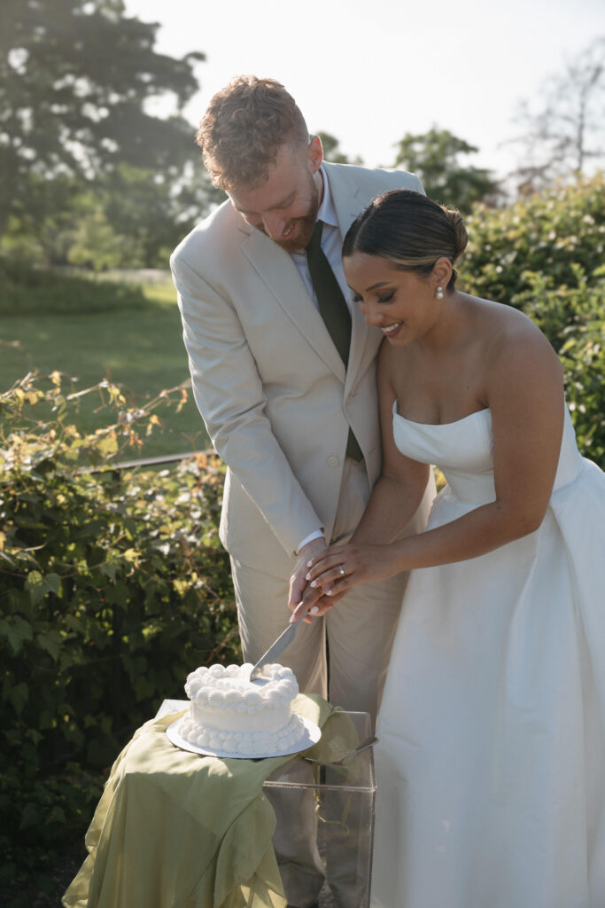 Documentary and editorial wedding photography from garden summer outdoor wedding at Eolia Mansion in Connecticut. Photos taken by Suz Lundeen Photo - destination wedding, family, and maternity photographer based in New England and the Midwest. Candid photo of bride and groom cutting their heart shaped wedding cake at their outdoor reception.