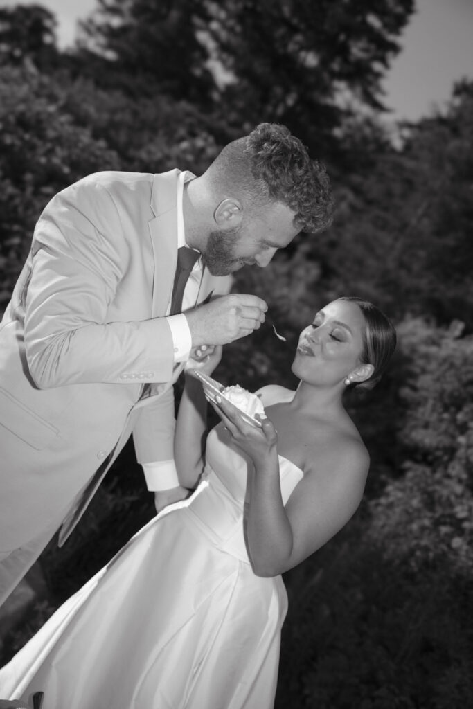 Documentary and editorial wedding photography from garden summer outdoor wedding at Eolia Mansion in Connecticut. Photos taken by Suz Lundeen Photo - destination wedding, family, and maternity photographer based in New England and the Midwest. Black and white photo of classic wedding picture of bride and groom feeding each other wedding cake.